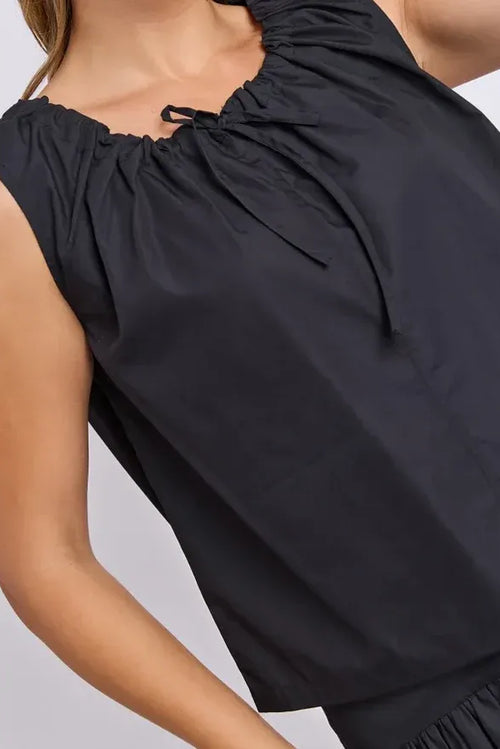 Close-up of a woman wearing a sleeveless black top with a gathered neckline and drawstring detail, paired with a matching black skirt.