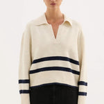 Woman wearing a cream sweater with navy stripes and black pants on a white background