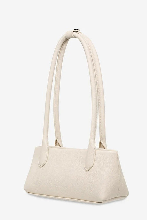 A small structured handbag in off-white pebbled leather with dual shoulder straps, shown from a side angle against a light gray background.