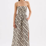 A woman modeling a sleeveless maxi dress with a black and off-white abstract wavy pattern, thin shoulder straps, and a side slit, photographed against a plain light gray studio background.