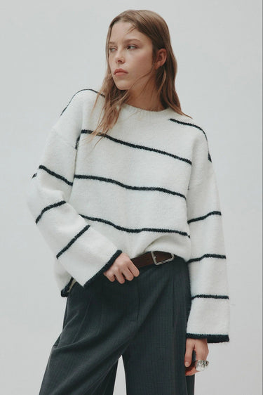Woman wearing a white sweater with black stripes against a plain background