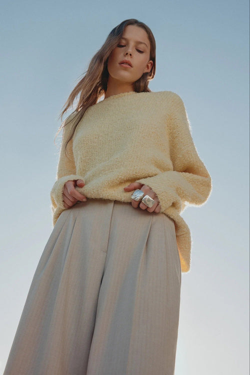 Woman wearing a yellow sweater and beige pants against a clear blue sky.
