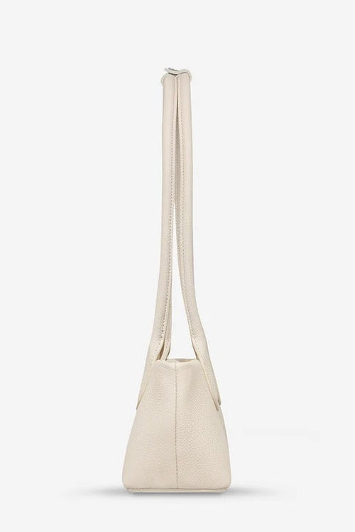 A light cream-colored pebbled leather shoulder bag with a single long strap, shown from a side profile view against a clean white background.
