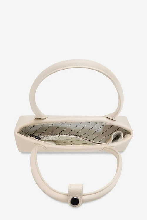 An open cream-colored leather handbag with a top handle and a circular lower handle, shown from a top-down view against a light gray background.