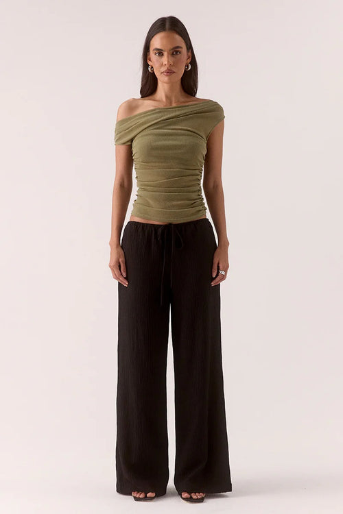 Woman wears a green ruched top and black pants