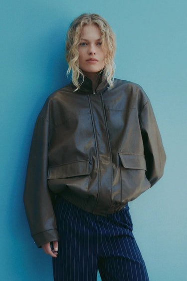 Person wearing a brown jacket and blue pants against a blue wall