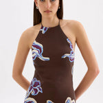 A model wearing a brown halter-neck dress with a purple and blue floral pattern, photographed against a plain light gray studio background.