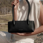 Person holding a black handbag in an outdoor setting