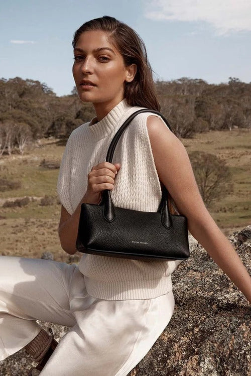Woman holding a black handbag in a natural setting