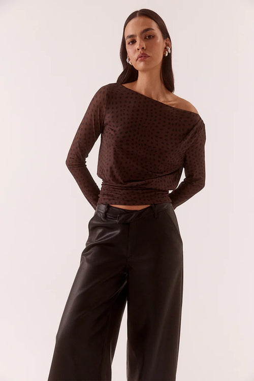 Woman wearing a brown off-shoulder top and black pants against a white background