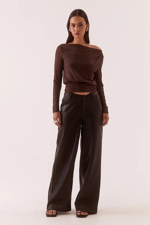 Woman wearing a brown off-shoulder top and dark pants on a white background