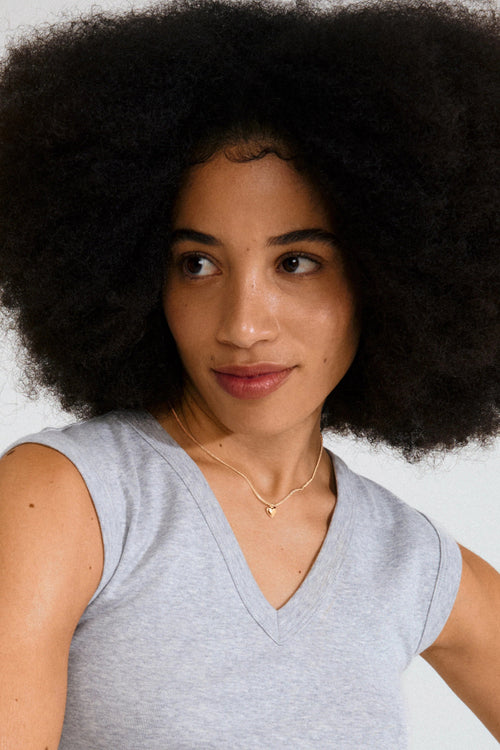 Woman with an afro wearing a gray sleeveless top against a plain background