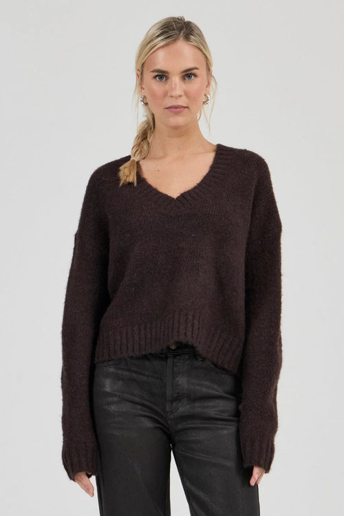 Woman wearing a brown sweater and black pants on a white background