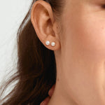 Close-up of a woman wearing pearl earrings with a neutral background