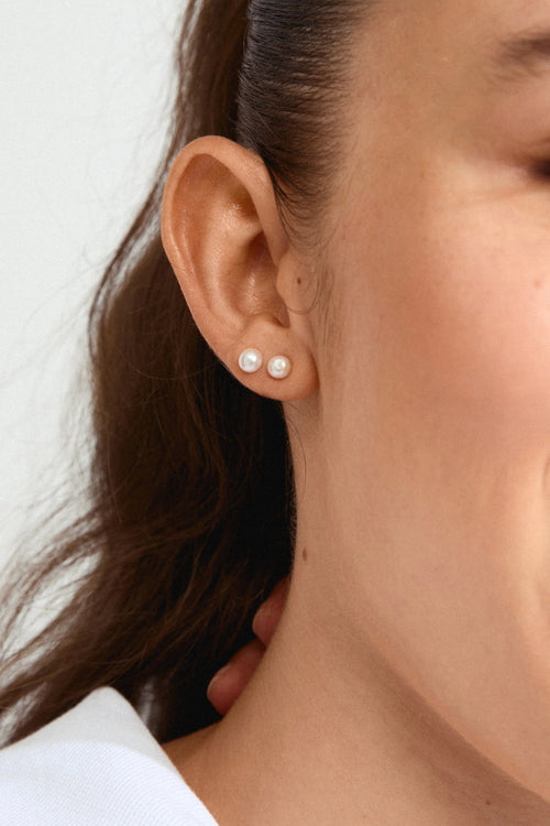 Close-up of a woman wearing pearl earrings with a neutral background