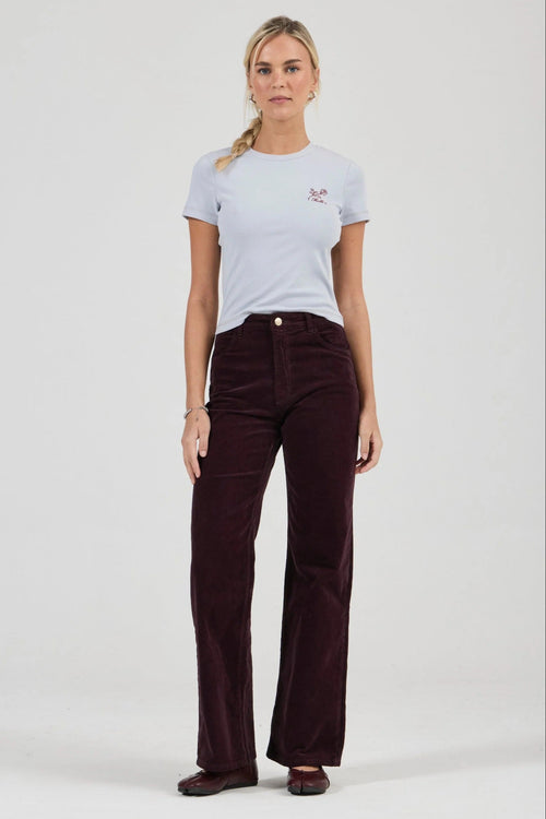 Woman wearing a light blue t-shirt and dark brown corduroy pants on a white background