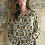 Woman wearing a patterned blouse against a textured stone wall