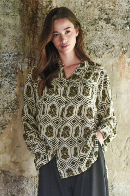 Woman wearing a patterned blouse against a textured stone wall