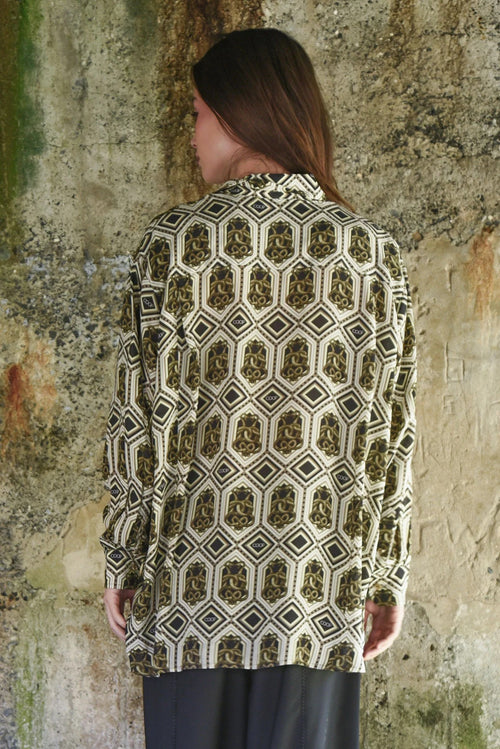 Woman wearing a patterned shirt against a textured wall.