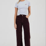 Woman wearing a light gray t-shirt and dark brown corduroy pants on a white background