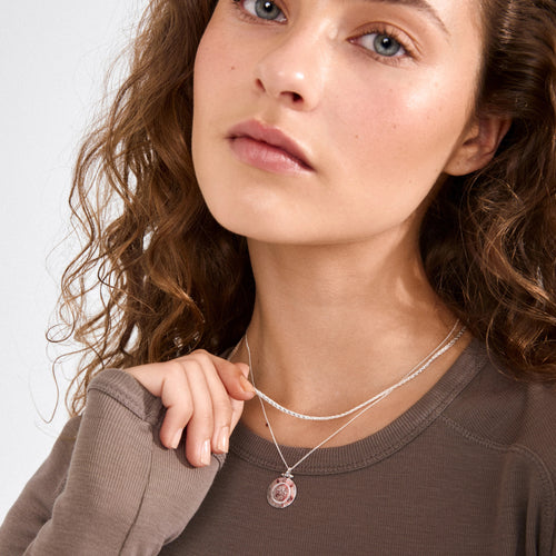 Woman wearing a necklace with a pink pendant on a plain background