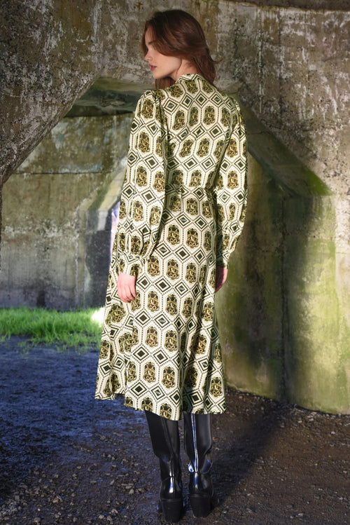 Woman wearing a patterned dress standing against a stone wall.