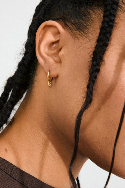Close-up of a person wearing a gold hoop earring with braided hair against a neutral background