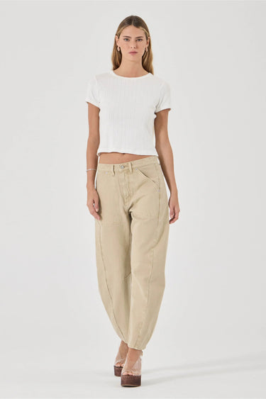 A model wearing a white ribbed short-sleeve crop top and beige wide-leg baggy pants, standing against a light gray studio background.