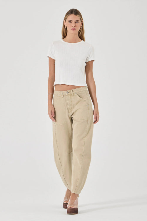 A model wearing a white ribbed short-sleeve crop top and beige wide-leg baggy pants, standing against a light gray studio background.