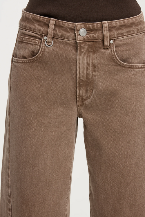 Close-up of a person wearing brown denim jeans with a faded wash, showing the front pockets, waistband, and button.