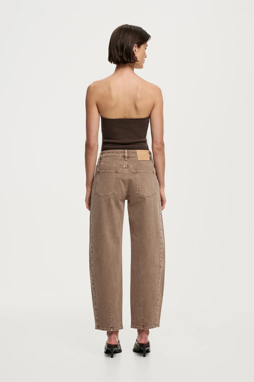 A model shown from the back wearing high-waisted, wide-leg brown jeans, a dark brown strapless top, and black pointed shoes against a plain light gray studio background.
