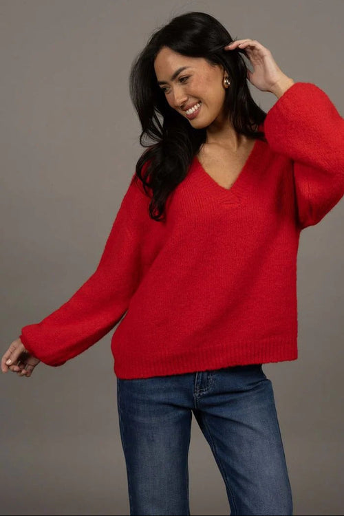 Woman wearing a red sweater and blue jeans against a gray background