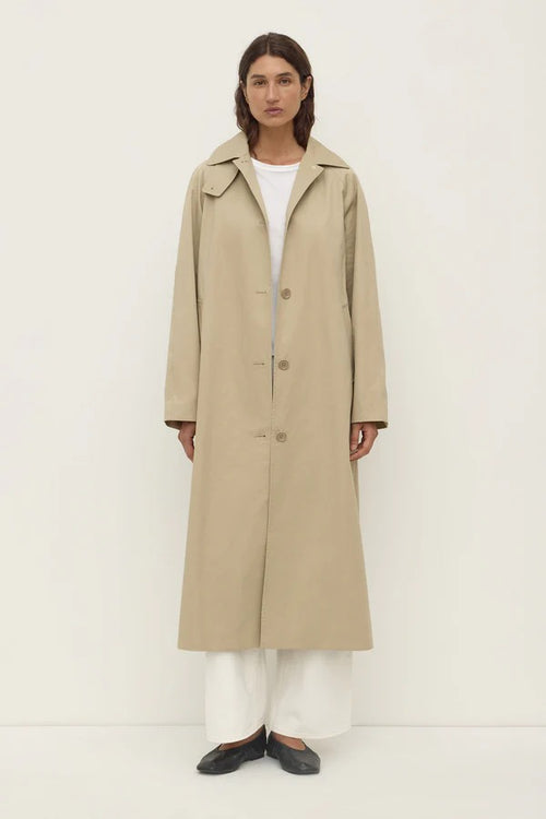 Person wearing a beige trench coat on a white background