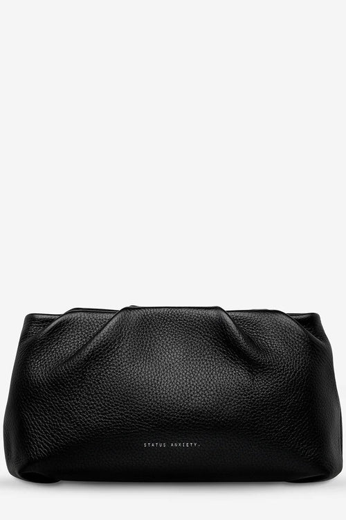 A black pebbled leather clutch bag with a gathered top edge and a small 'STATUS ANXIETY.' logo printed in white near the bottom center, set against a plain white background.