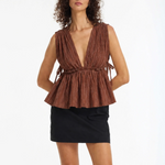 A woman modeling a sleeveless brown pleated top with a deep V-neck and gathered waist, paired with a black mini skirt, against a plain white studio background.