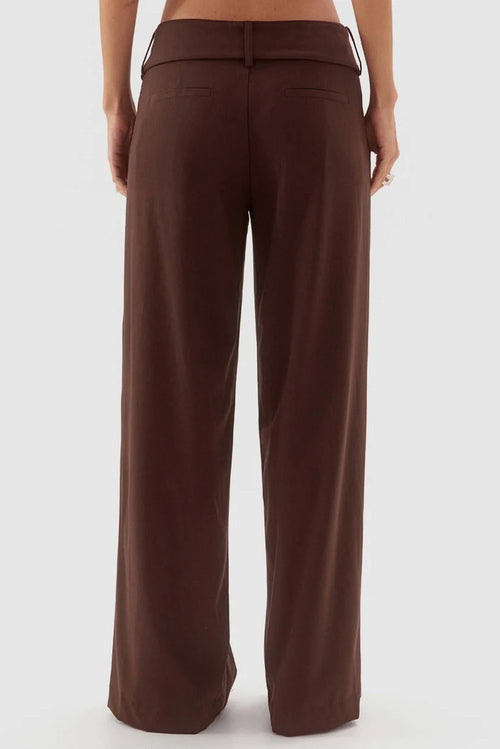 A person shown from the back wearing high-waisted, wide-leg brown pants against a light gray studio background.