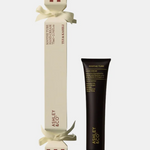 Asley & Co. Hand Cream shown with its cream-colored gift box tied with a white ribbon and a black squeeze tube with gold lettering, on a light gray background.