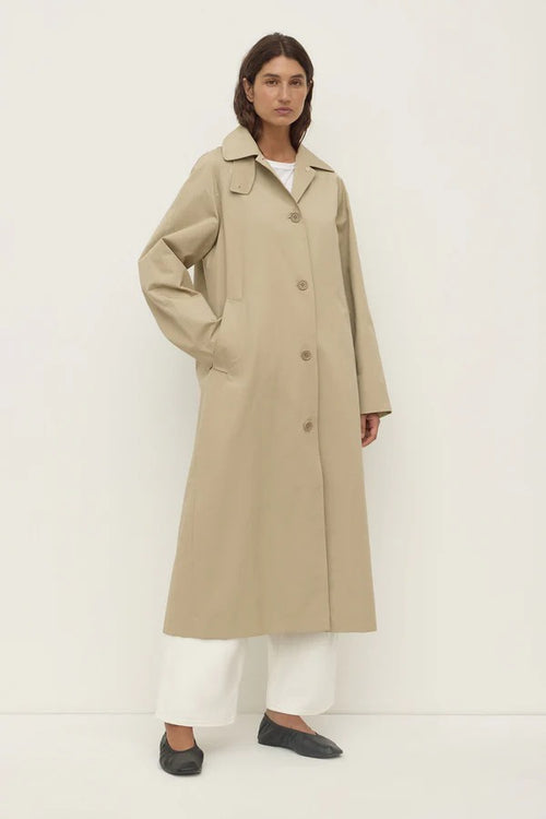 Person wearing a beige trench coat on a white background