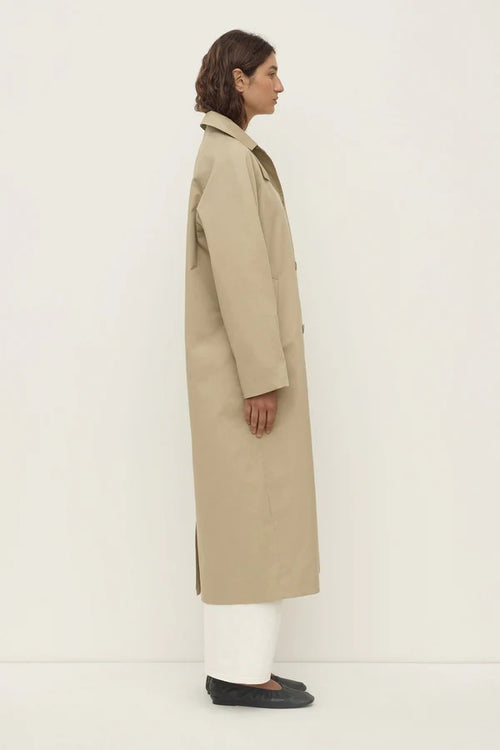 Person wearing a beige trench coat on a white background