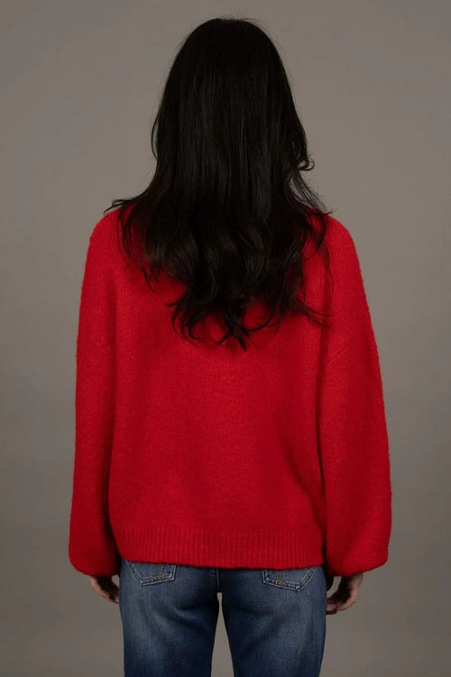 Person wearing a red sweater and blue jeans against a gray background