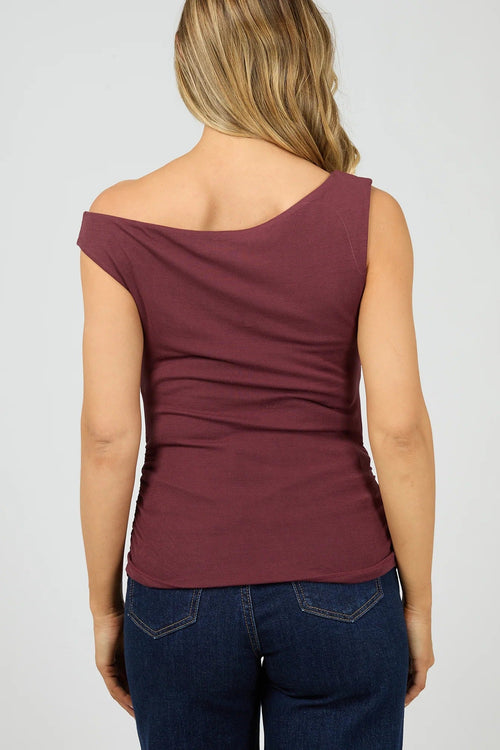 Woman wearing a burgundy off-shoulder top and blue jeans on a plain background