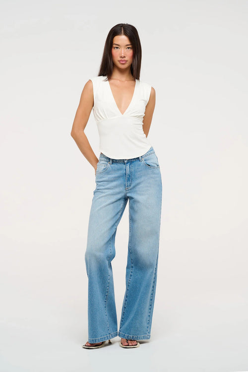 Model wearing mid indigo wide-leg jeans with a mid-rise waist, styled with a white sleeveless V-neck top and sandals.