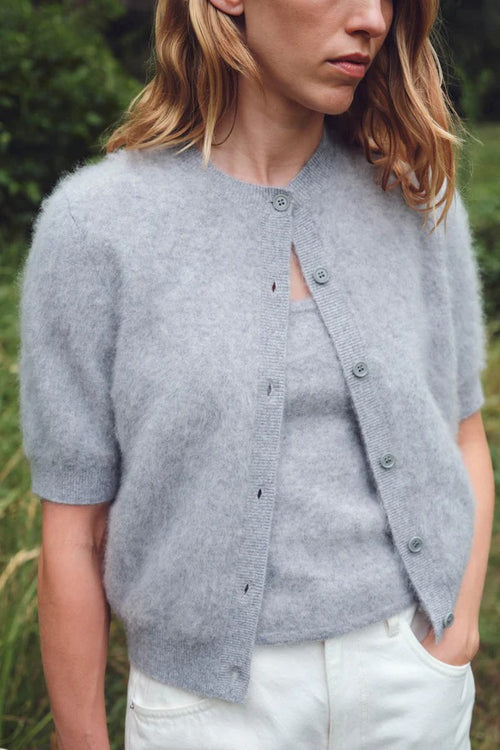 Person wearing a gray cardigan over a white shirt in a natural setting