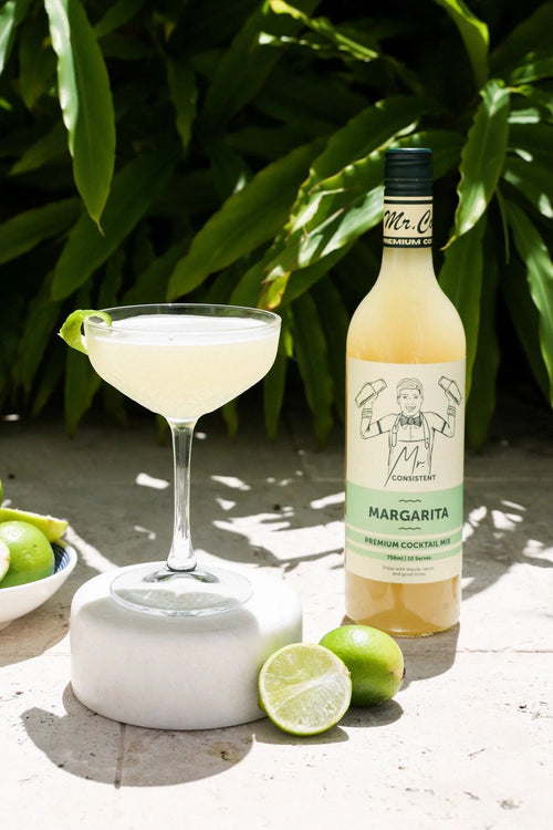 Margarita bottle with a glass of margarita and limes on a natural background