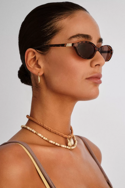 Woman wearing sunglasses and layered necklaces against a plain background