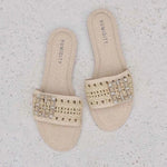 Pair of beige sandals with embellishments on a textured white surface
