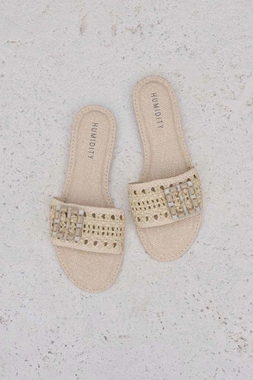 Pair of beige sandals with embellishments on a textured white surface