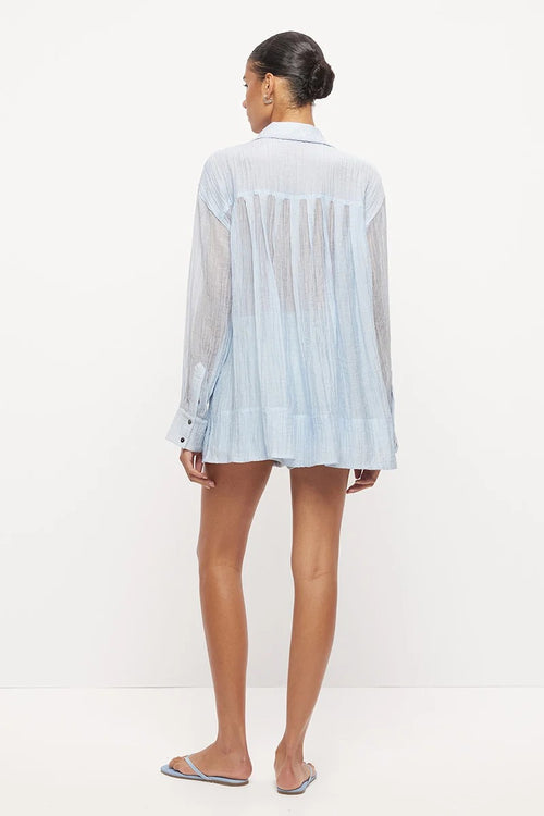 Model wearing a light blue semi-sheer oversized button-up shirt with long sleeves, paired with matching drawstring shorts and flat sandals.