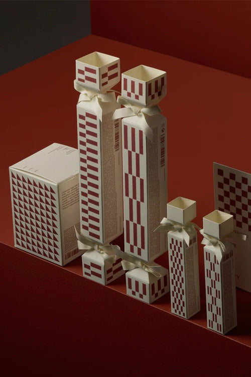 A set of cream-colored Christmas crackers and boxes decorated with a red-and-white checkered pattern, arranged on a dark red geometric platform.