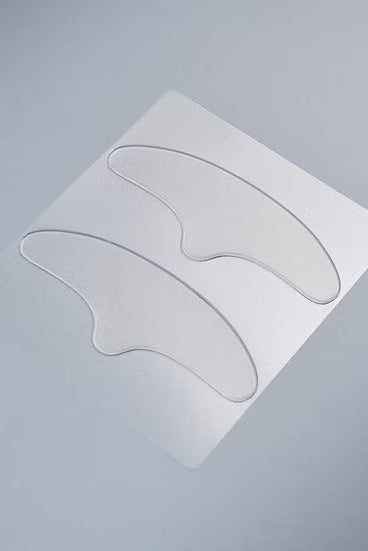 Two clear, curved adhesive patches on a white backing card, photographed on a smooth, light gray surface.